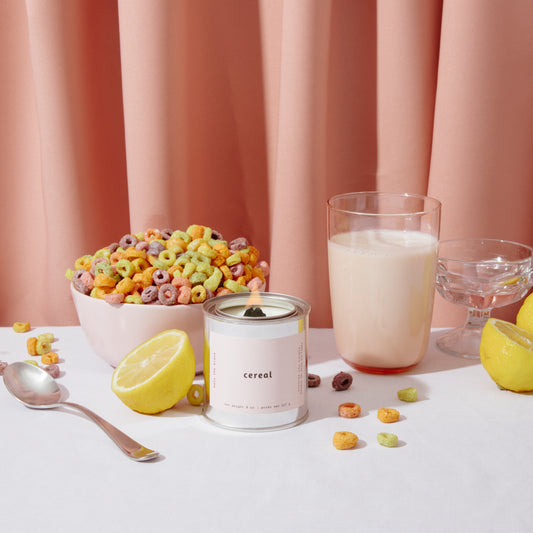 mala cereal candle with a bowl of fruit loops, a glass of milk, a spoon, and lemons