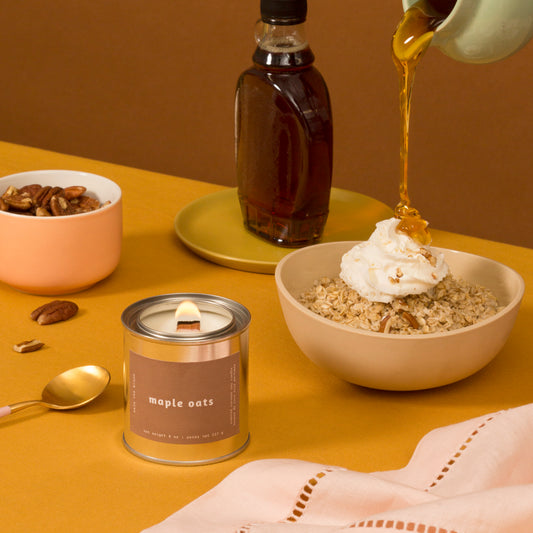 mala maple oats candle sitting next to a bowl of oats topped with whipped cream and maple syrup