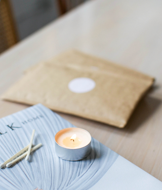 a tealight candle lit next to matches and our brown packaging sleeve on top of a blue book